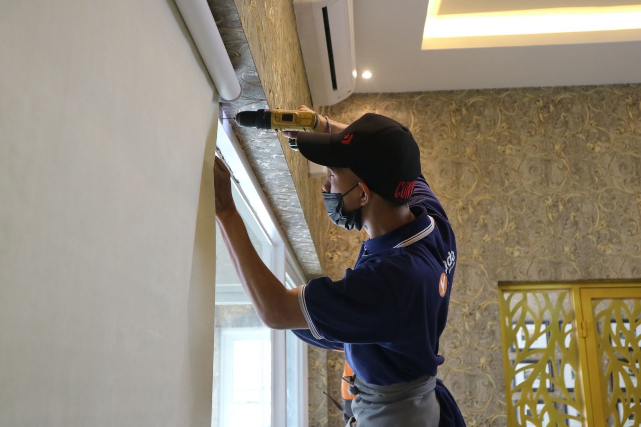 who-we-are A worker using a drill to install window blinds in an indoor setting.